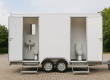 Een geopende mobiele toiletwagen op locatie met zicht op het hygiënische interieur, uitgerust met spoeltoiletten, een wastafel en een spiegel